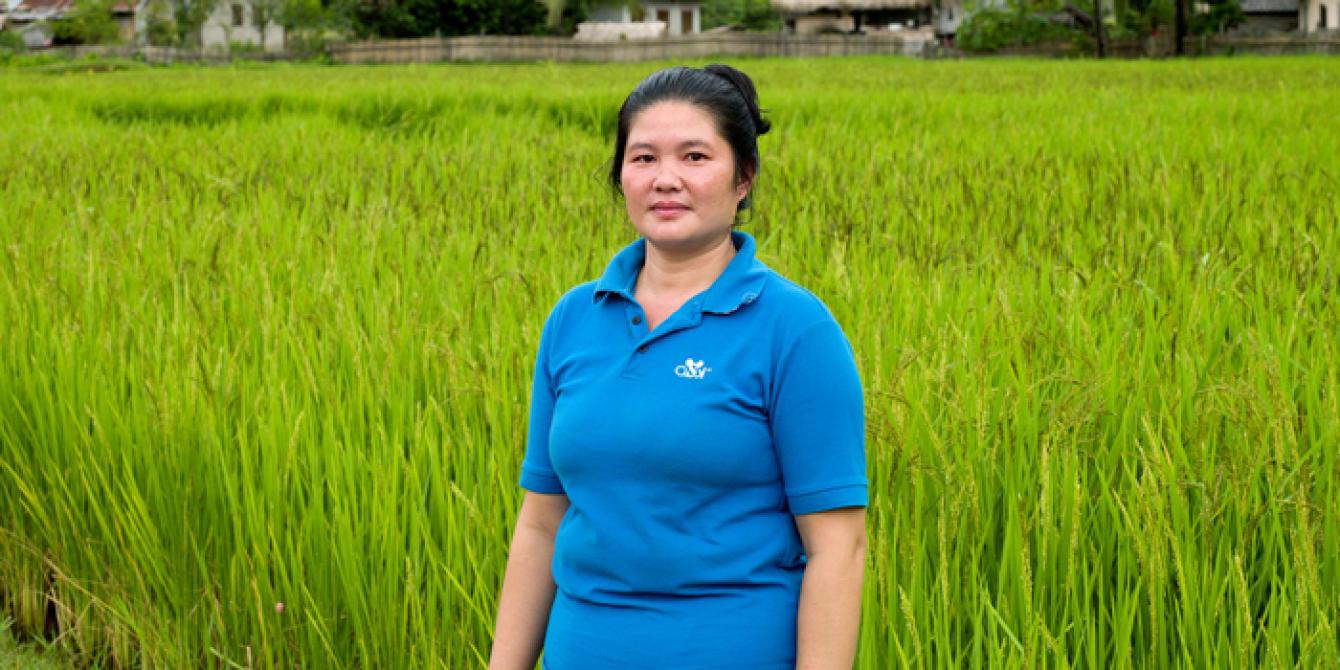 One Rice Yield at a Time woman in blue standing nest to a green rice field
